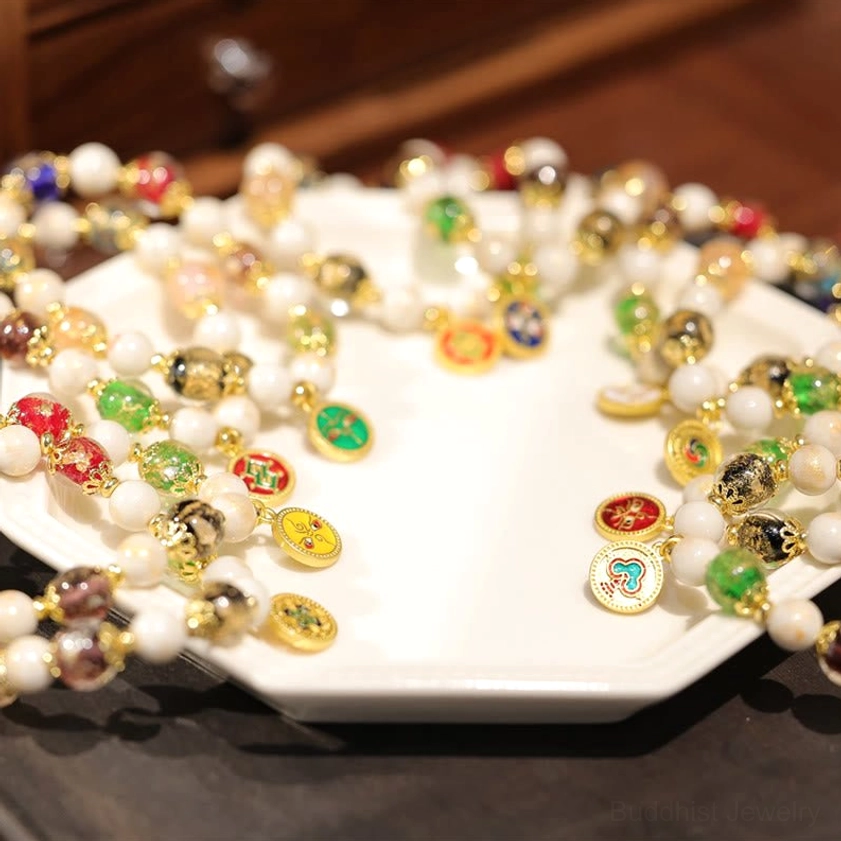 Multiple Buddhist wealth charm bracelets with various enamel deity faces scattered on octagonal white plate with wooden background