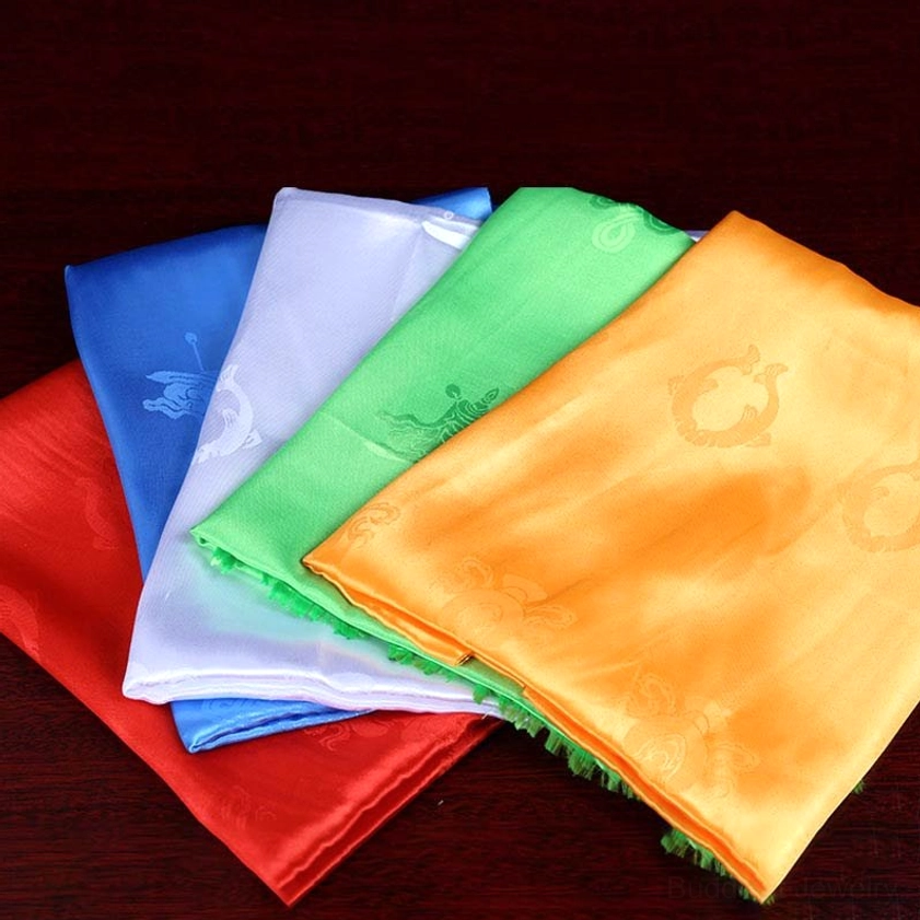 Loose Buddhist khata scarves in five colors displayed oblique top-down view on dark wooden surface with embossed ceremonial patterns