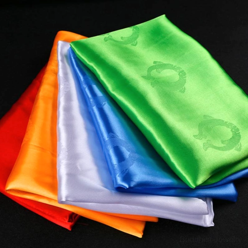 Five-color khata scarf set oblique top-down view on dark background with vibrant solid hues and embossed circular spiritual designs