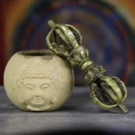 Handmade five-prong copper vajra dorje with dragon motifs, displayed on Buddhist altar with ceramic vessel