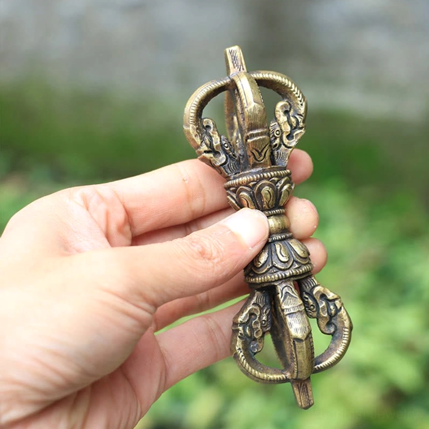 Close-up hand-held view of five-prong copper vajra dorje with natural outdoor lighting showing carved details