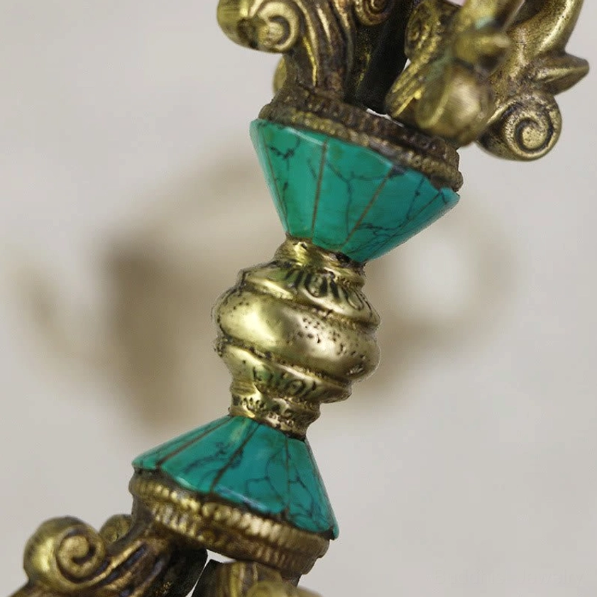 Close-up side view of vajra dorje showing stacked turquoise and brass segments with carved patterns