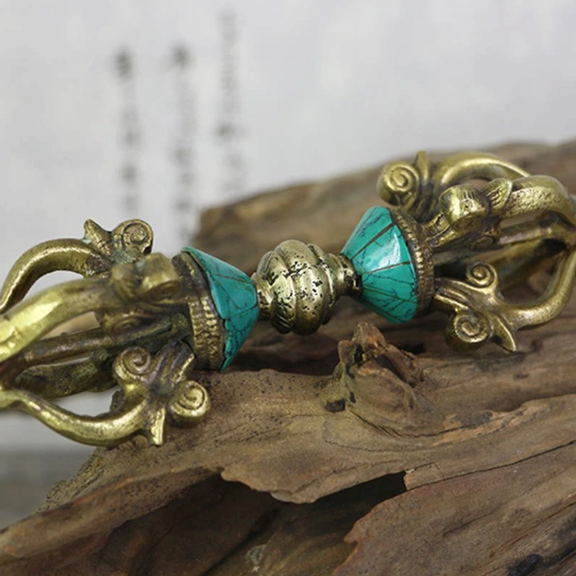 Five-prong vajra dorje on driftwood wood surface highlighting clear turquoise inlays and polished brass