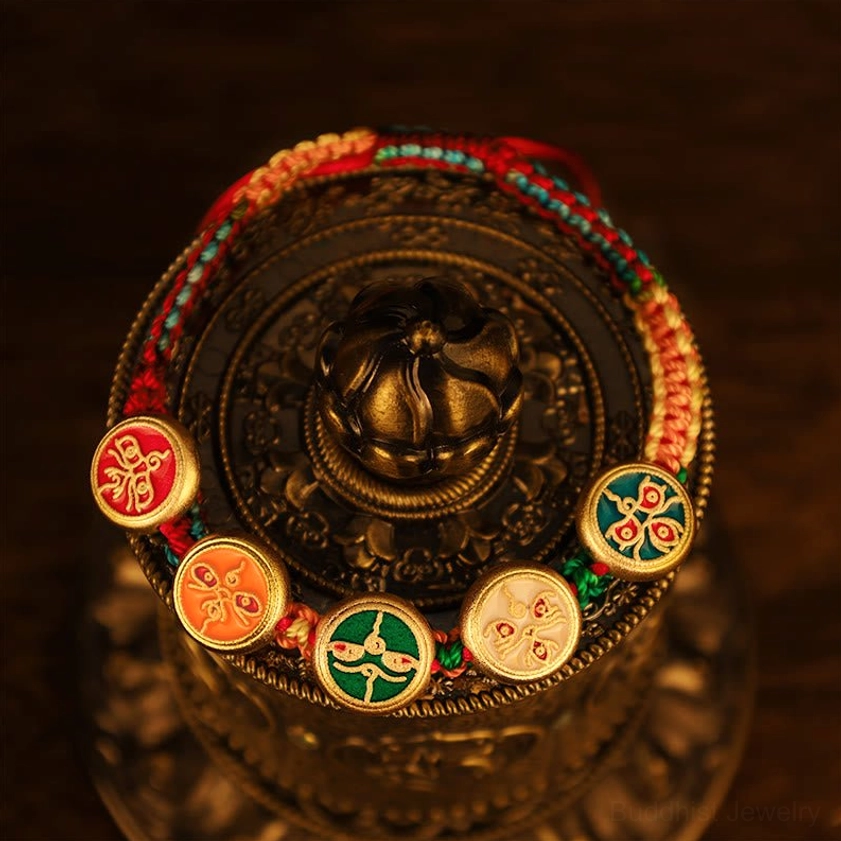 Close-up detail of five wealth deities bracelet charms arranged on vintage Tibetan brass container showing intricate enamel work