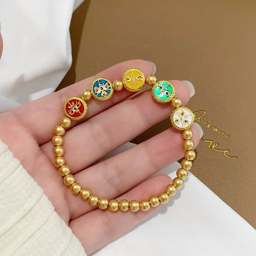 Hand-held close-up of five wealth gods Buddhist bracelet showing distinct matte gold beads and colorful fortune charms