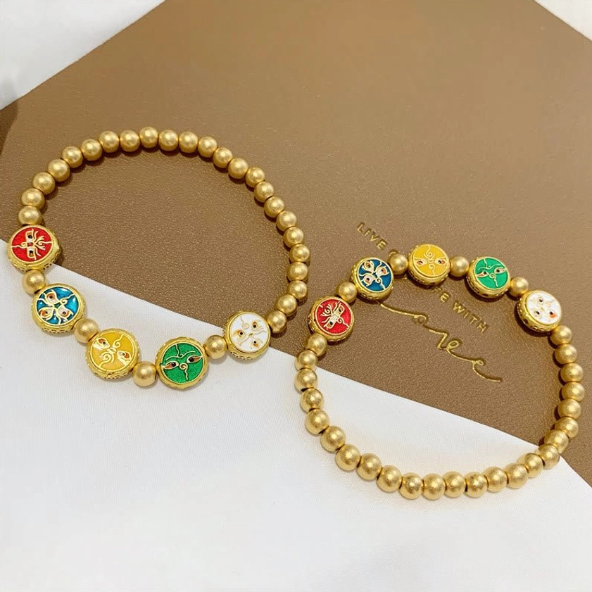 Two matching five wealth gods copper bracelets with enamel fortune charms on branded brown linen desktop