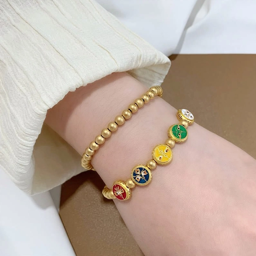 Five wealth gods bracelet worn on clothed arm showing matte gold beads and colorful enamel prosperity charms
