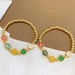 Pair of five wealth gods copper beaded bracelets with colorful enamel fortune charms displayed on branded brown linen