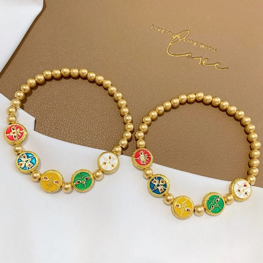 Pair of five wealth gods copper beaded bracelets with colorful enamel fortune charms displayed on branded brown linen