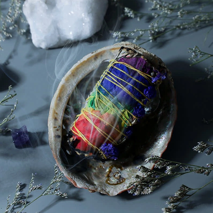 Multicolor dried floral smudge stick wrapped in yellow twine resting in pearl abalone shell