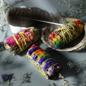 Handcrafted floral smudge stick ritual set with colorful daisy, red rose, and rainbow flowers bound with yellow twine on decorative tabletop