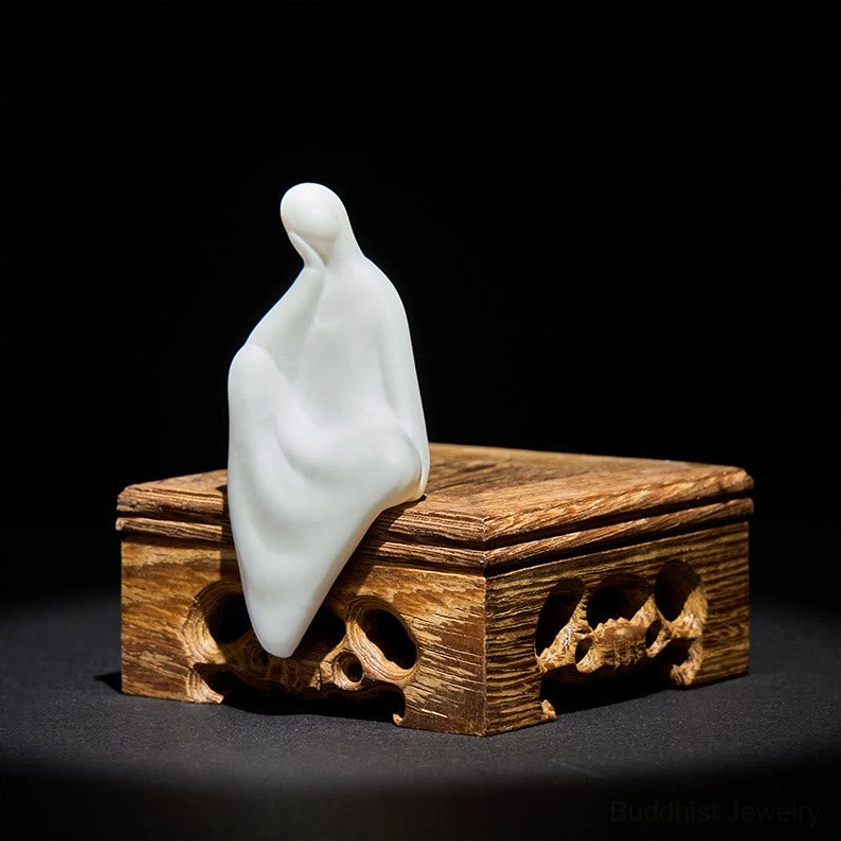 Zen Buddha meditation sculpture in pure white ceramic with dark wooden carved base, right front three-quarter angle highlighting craftsmanship