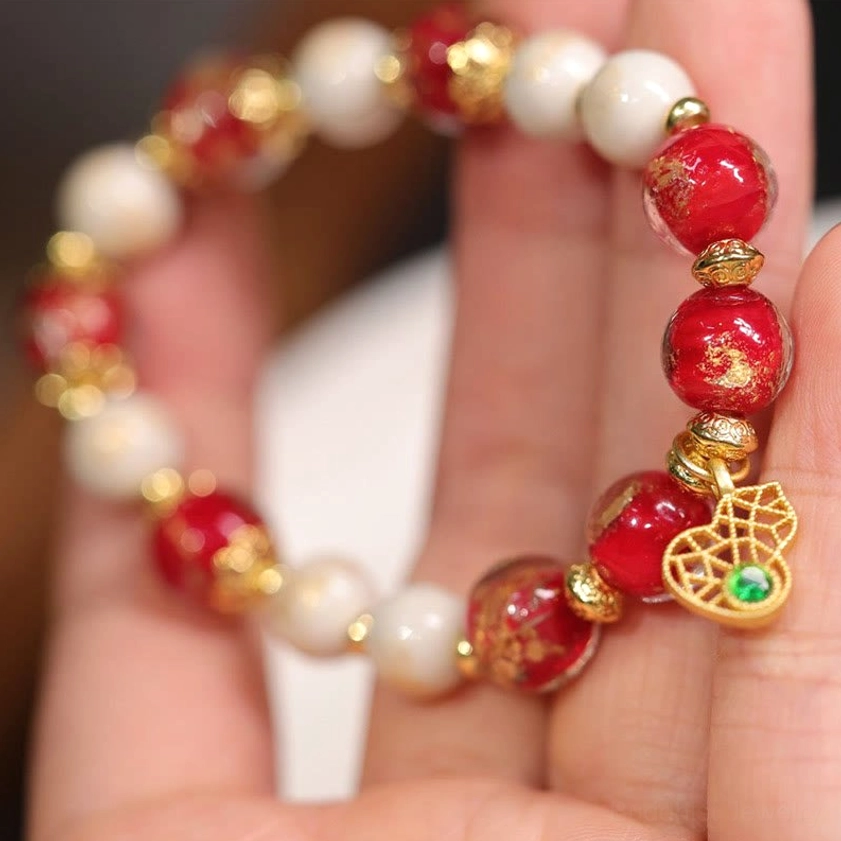 Hand-held close-up of incense ash porcelain and Liuli glass bead bracelet with shiny red beads and hollow gold gourd charm