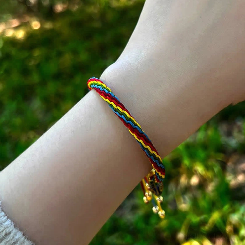 Multicolor braided fortune bracelet on model wrist outdoors with green background and gold charm