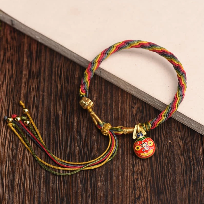 Multicolor fortune string bracelet with gold Swallowing Beast charm and protective red cord on desk with paper