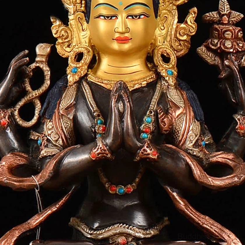 Detailed frontal view of four-armed Avalokitesvara copper statue showing facial painting, beaded necklaces, and colored gem inlays