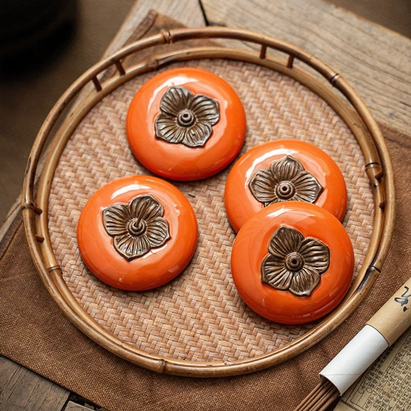 Set of four handcrafted ceramic persimmon incense holders arranged on bamboo woven tray with incense sticks and decorative scroll