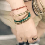 Four-gemstone Buddhist triple wrap bracelet worn on both wrists showing red agate, black onyx, green agate and white agate stones with brass accents in casual daily wear