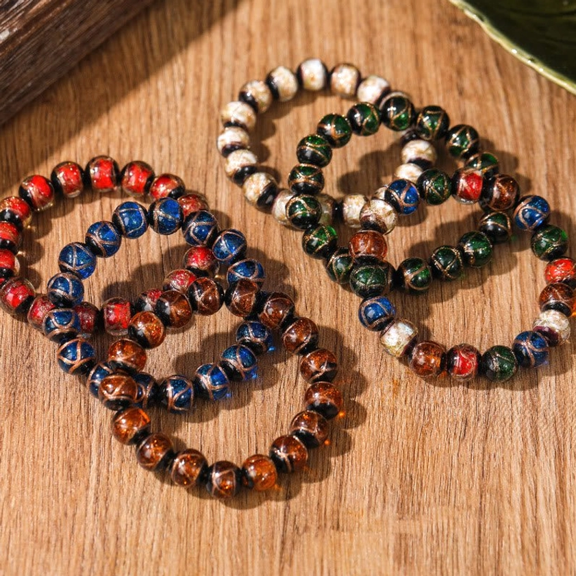 Four sets of handmade liuli glass Buddhist bracelets in various colors displayed on wooden desk with green leaf decoration