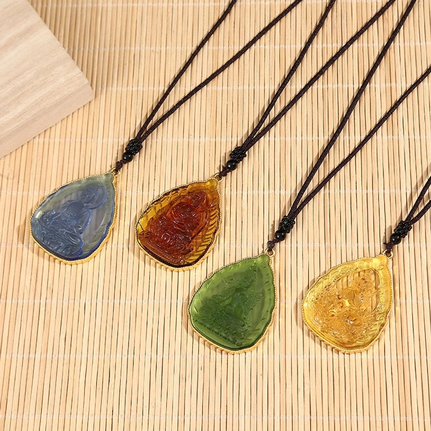 Set of four colorful Buddhist crystal Buddha pendants with black beaded wax cords arranged on bamboo mat background, showing variety of crystal colors for spiritual meditation