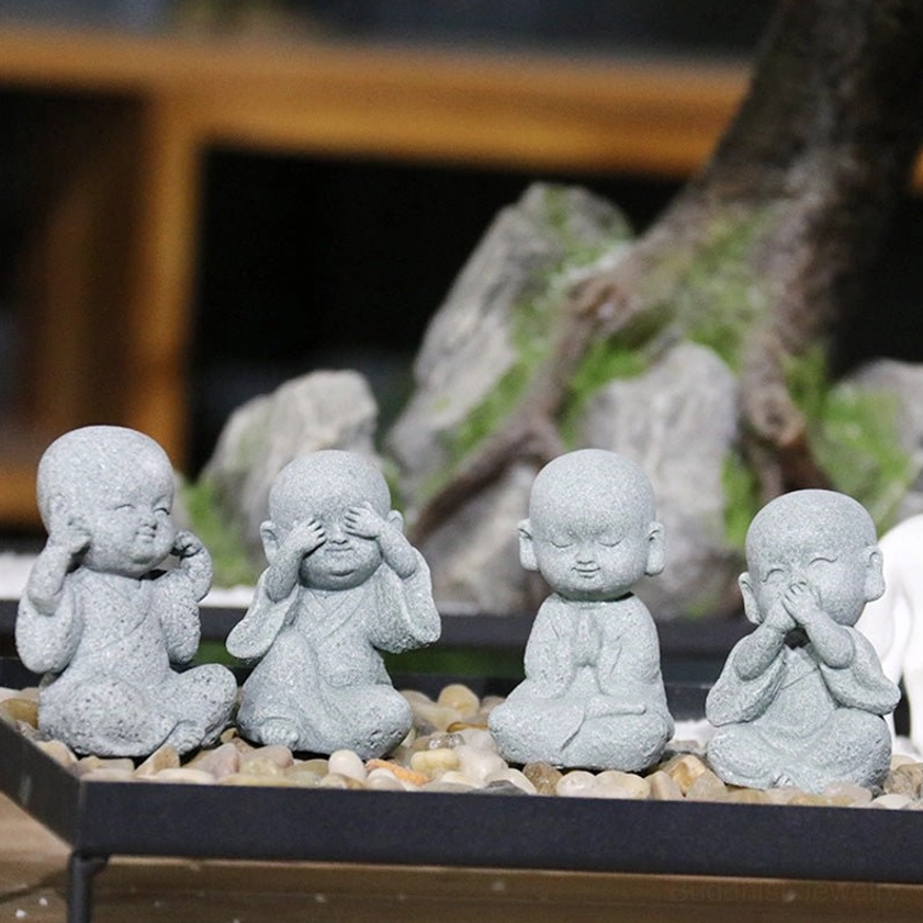 Collection of four mini monk Buddha figurines in zen rock garden display tray showing various meditation poses