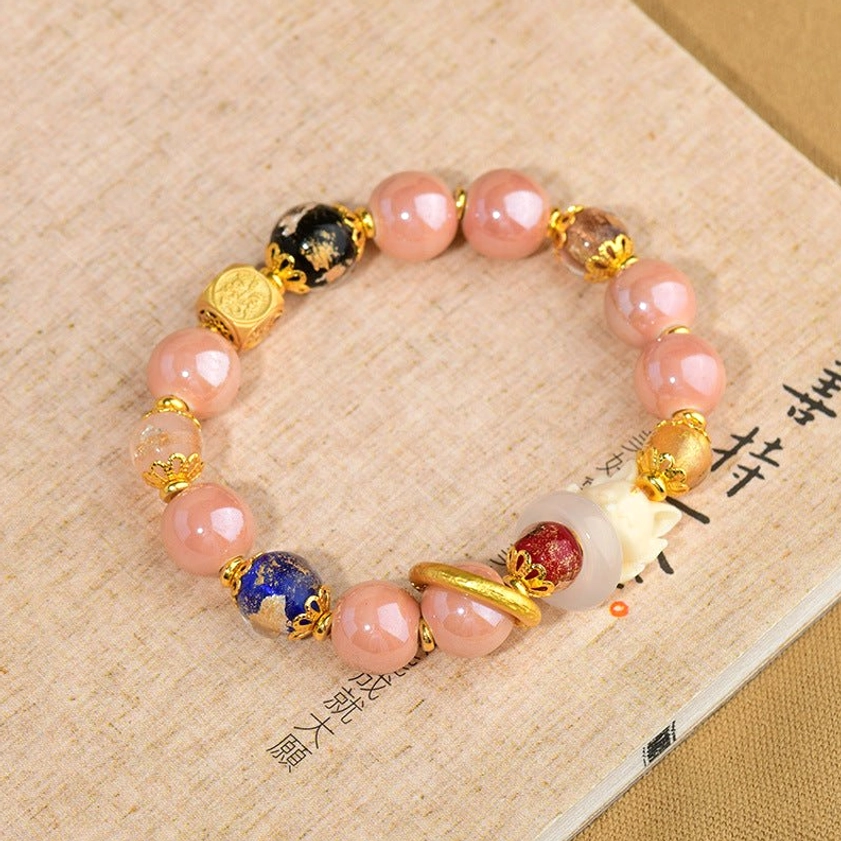 Protection prayer bead bracelet featuring nine-tailed fox amulet, pink glass beads, gold hardware, and mixed decorative beads, displayed with Chinese spiritual text