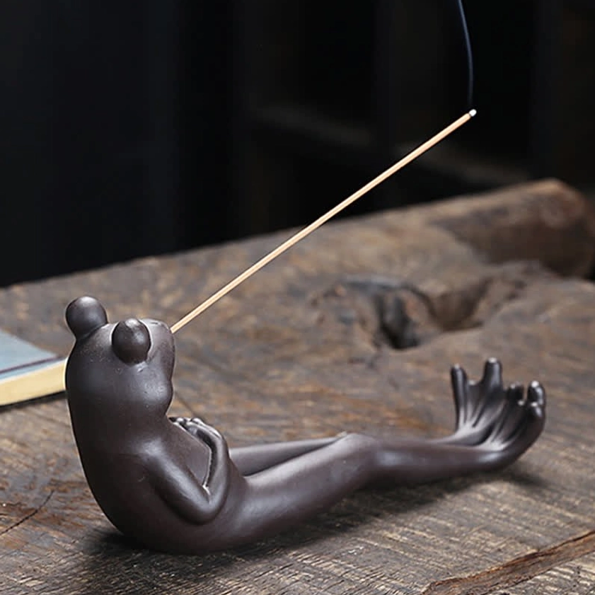 Meditation frog incense burner with hand pose detail, incense stick positioned in mouth, wooden table backdrop