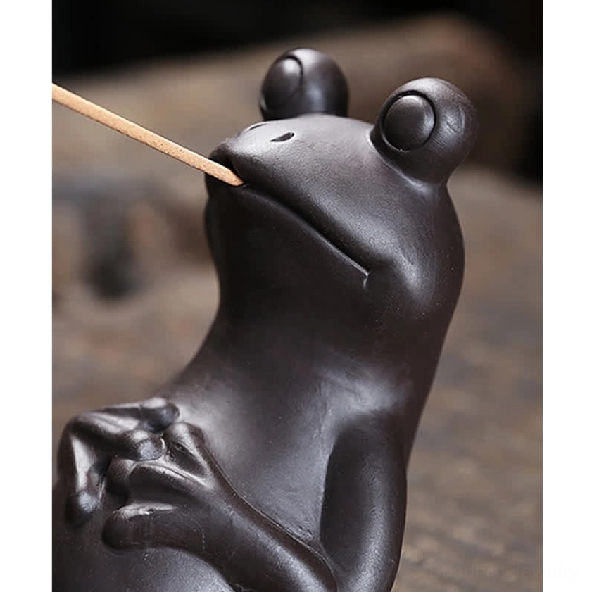 Extreme close-up of handcrafted frog incense burner mouth detail holding burning incense stick