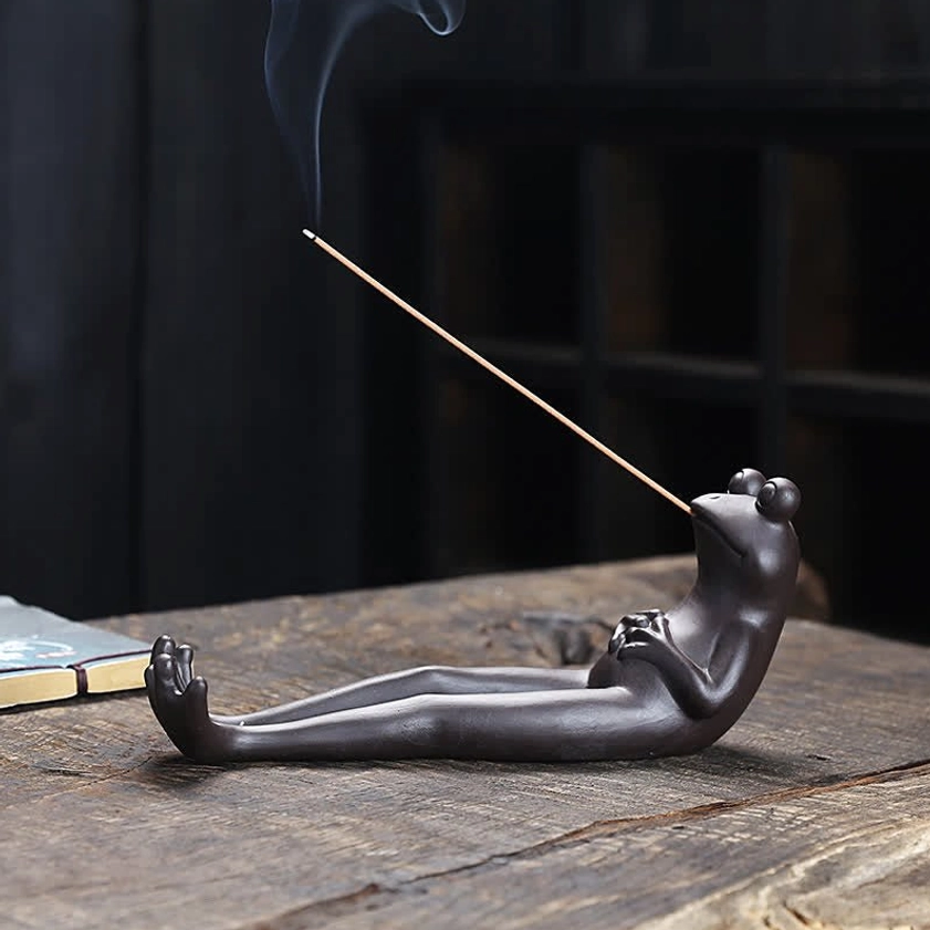 Low angle side view of handmade ceramic frog incense holder with fragrant incense smoke, tea table setting