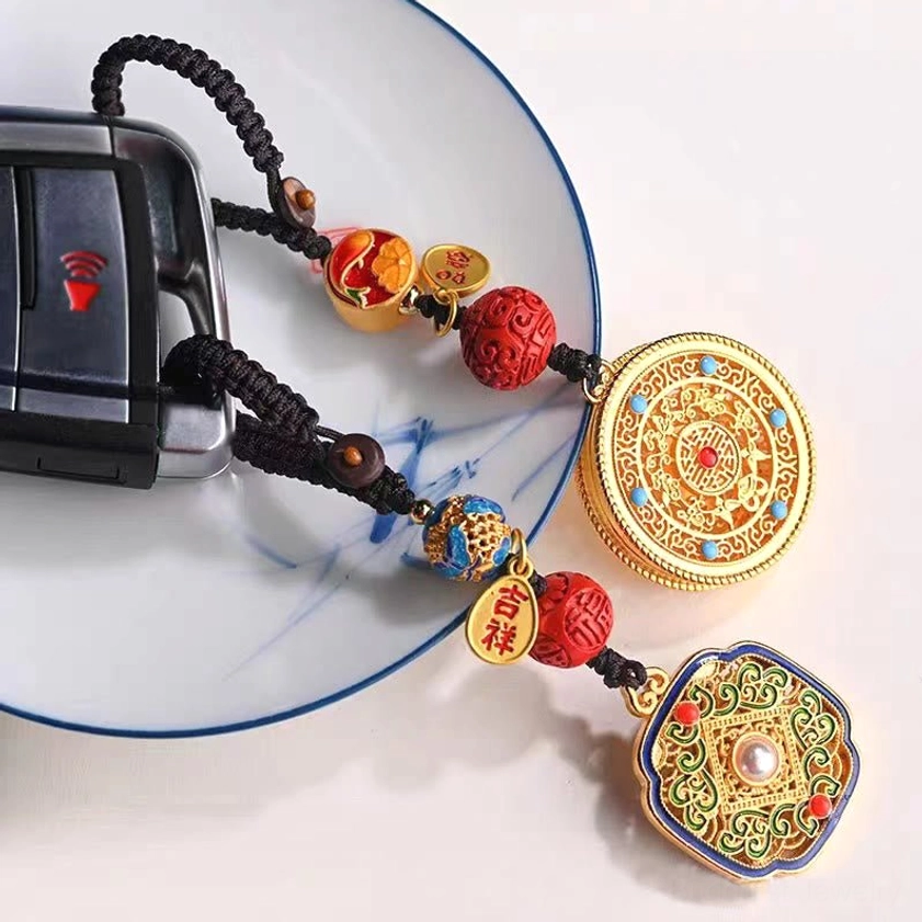 Buddhist blessing keychain attached to car key on blue and white porcelain plate showing auspicious metal tag with red and blue decorative beads