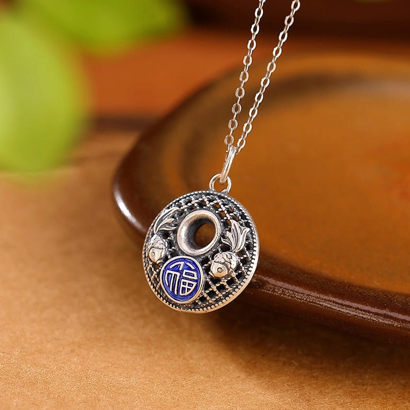Silver fu character peace buckle pendant side oblique view showing filigree texture on wooden tray