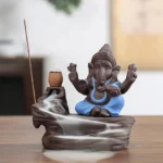 Ganesha backflow incense burner with blue deity figure on purple clay base, showing cascading aromatic smoke waterfall effect