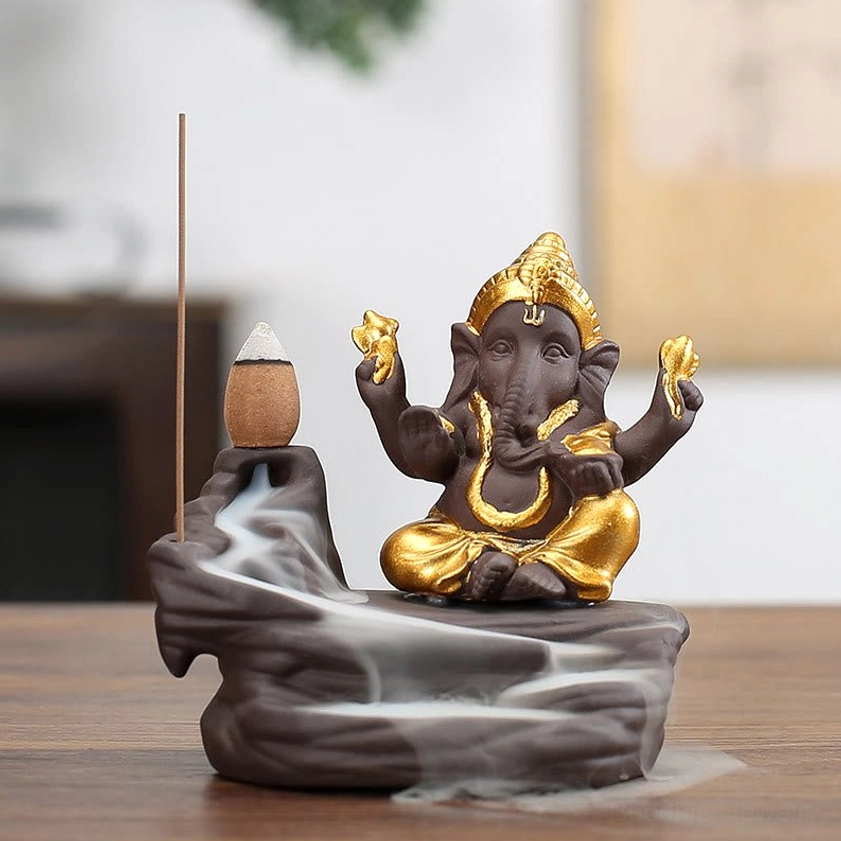 Gold-plated Ganesha backflow incense burner on purple clay base with visible smoke cascade, front view