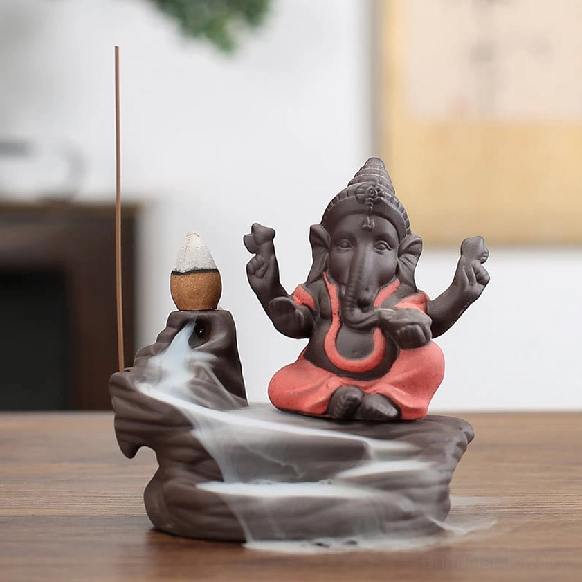 Orange Ganesha incense holder with backflow smoke fountain on dark purple clay ceramic base, front perspective