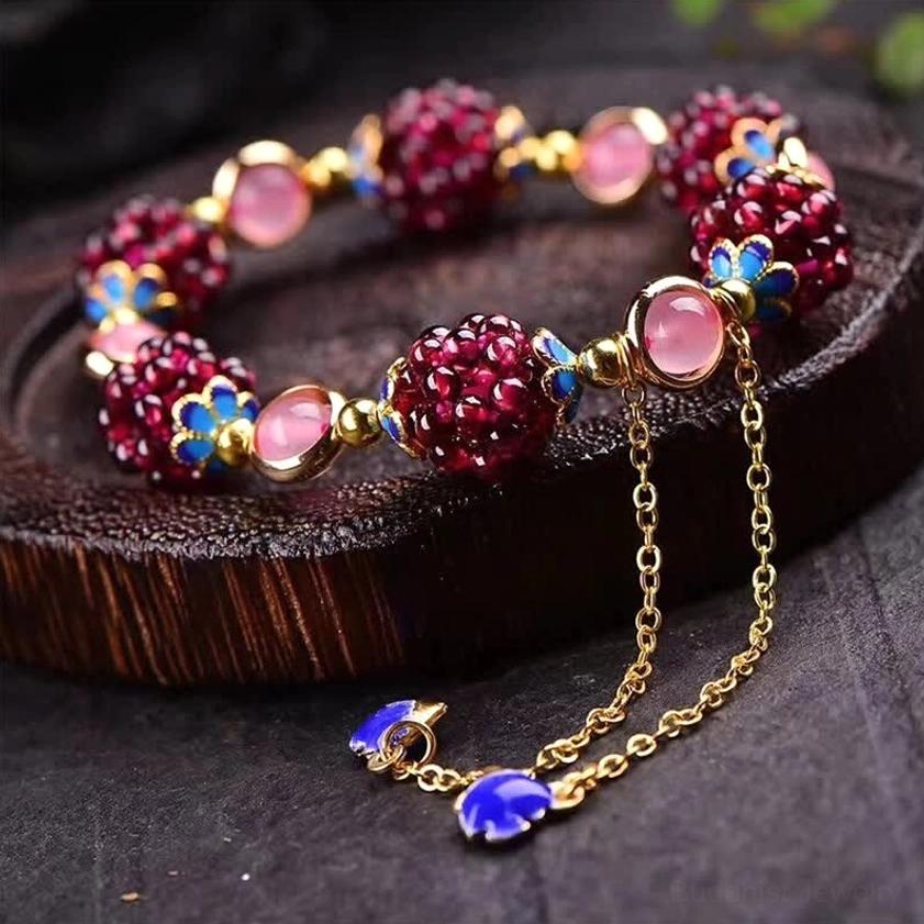 Garnet amethyst Buddhist healing bracelet with gold hardware and blue enamel drop charms displayed on wooden tray
