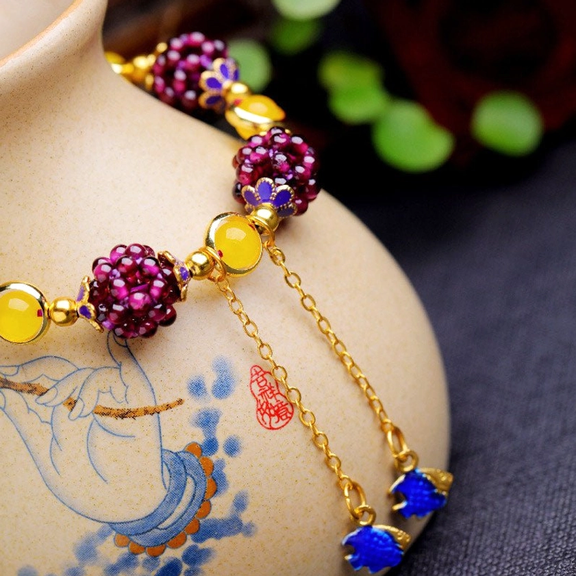 Close-up view of garnet cluster bracelet with amethyst and enamel flower beads on ceramic display
