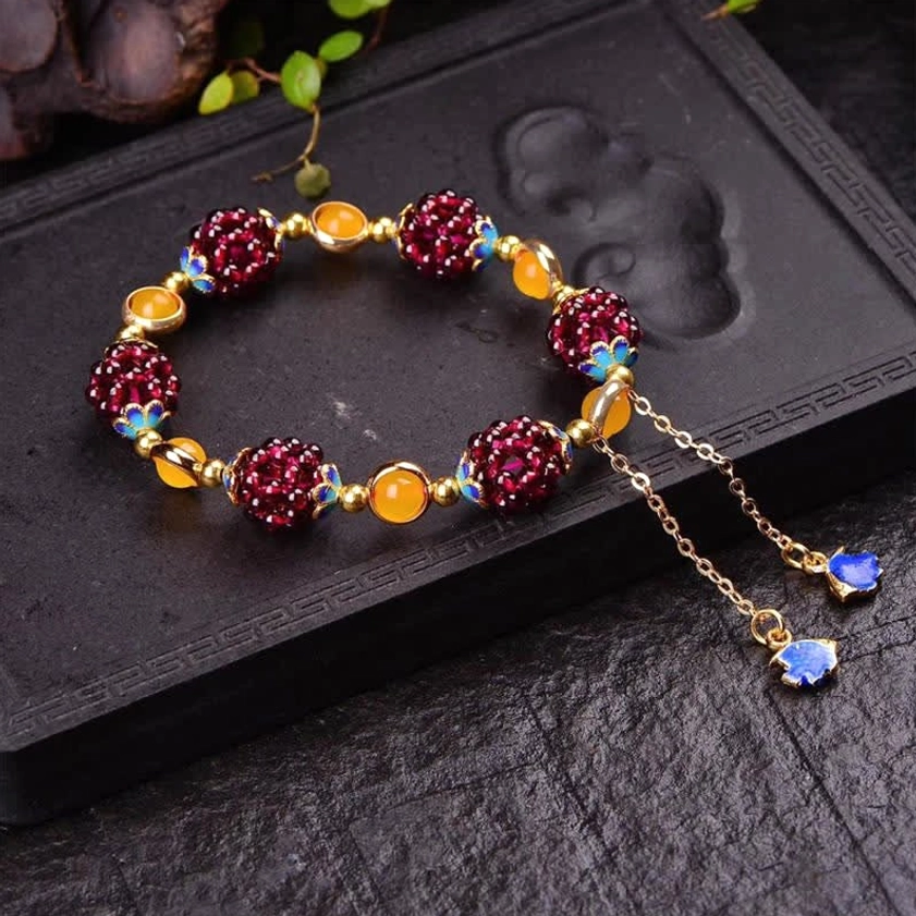 Single garnet amethyst bracelet with double extender chains and blue enamel drops on carved wooden display