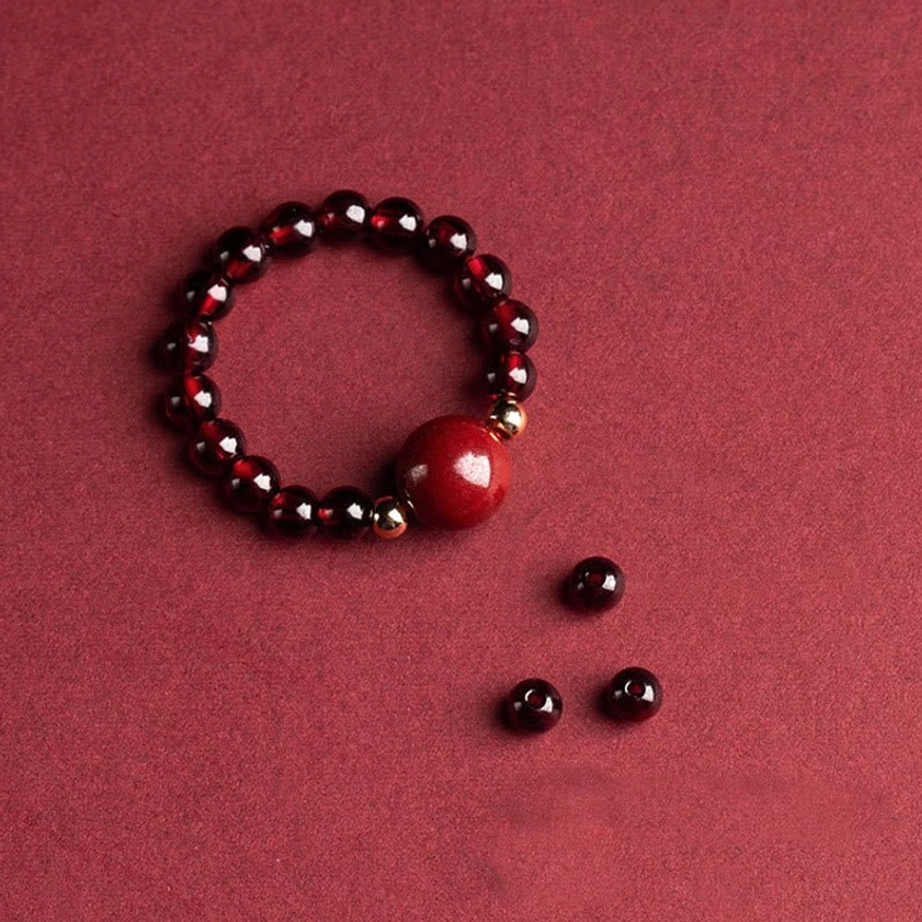 Garnet cinnabar focal bead Buddhist bracelet with large polished round cinnabar centerpiece, dark lustrous beads, and loose matching beads on wine-red background