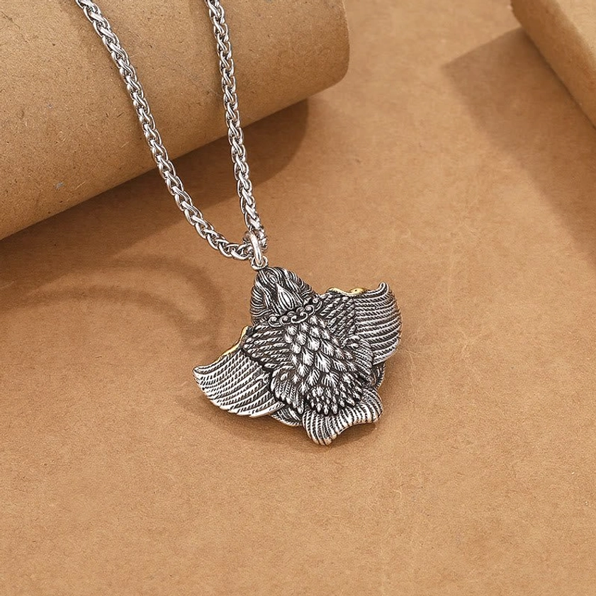 Silver tone Garuda Bird Buddhist symbol pendant with realistic feather carvings on brown background