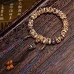 Carved Garuda camel bone protection bracelet with vibrant dual tassels and colorful inlaid beads, displayed on dark wood surface