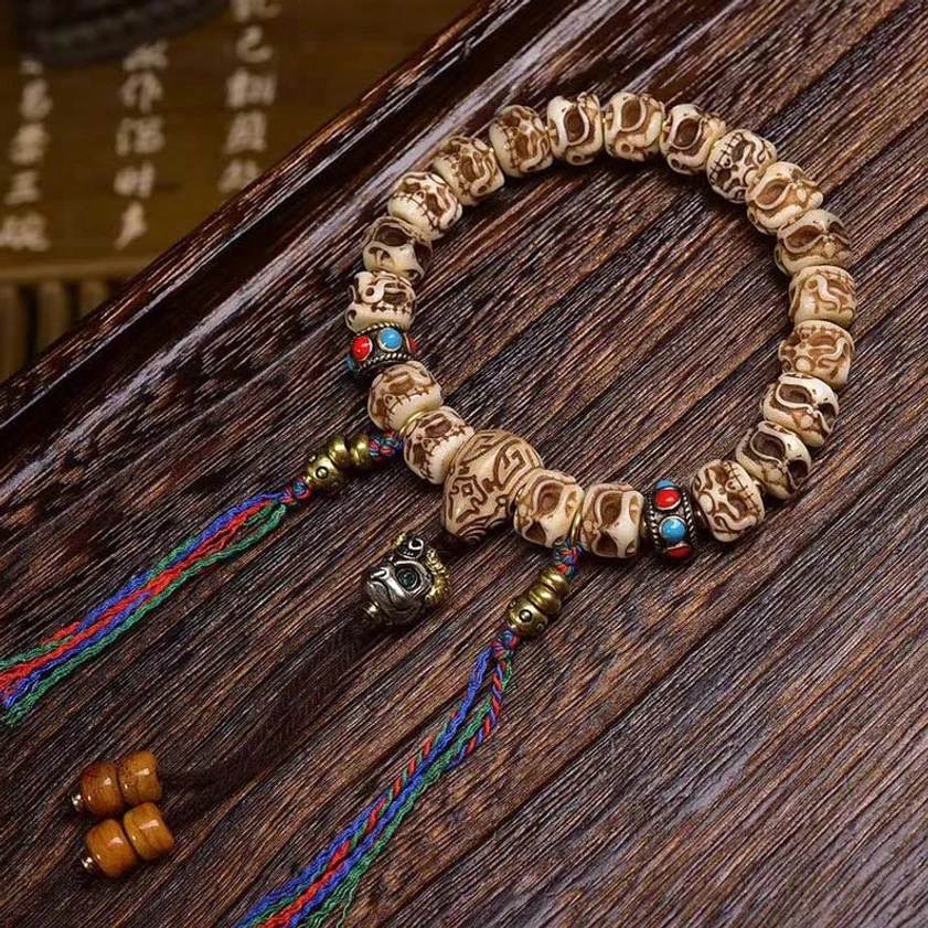 Carved Garuda camel bone protection bracelet with vibrant dual tassels and colorful inlaid beads, displayed on dark wood surface