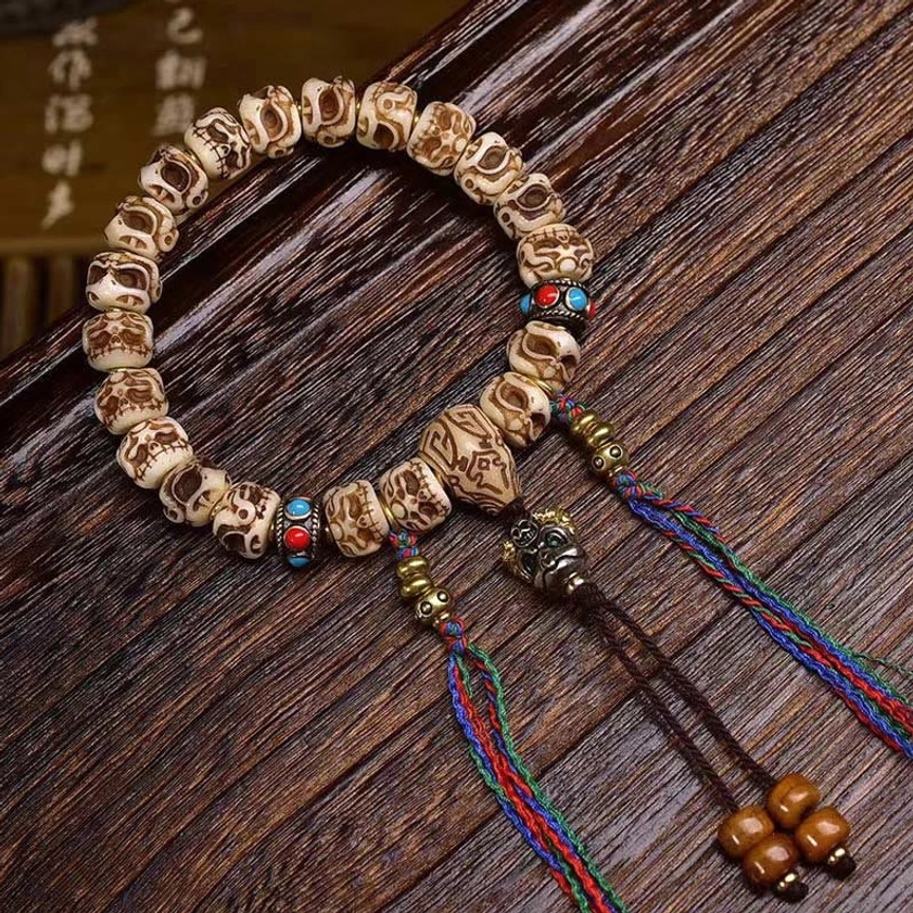 Buddhist Garuda protection bracelet detail showing metal charm, woven tassel pendants, and wooden bead accents