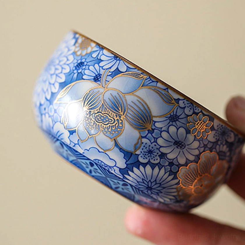 Close-up handheld view of gilded porcelain teacup with large lotus and dense blue floral background
