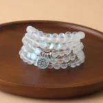 108 glitter stone mala beads bracelet with lotus charm displayed on wooden tray, iridescent frosted beads with silver spacers and engraved lotus pendant