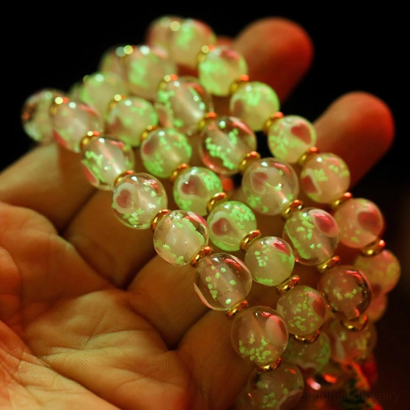 Handheld close-up view of luminous green glow-in-the-dark Buddhist bracelet with enamel charm pendants held on human palm