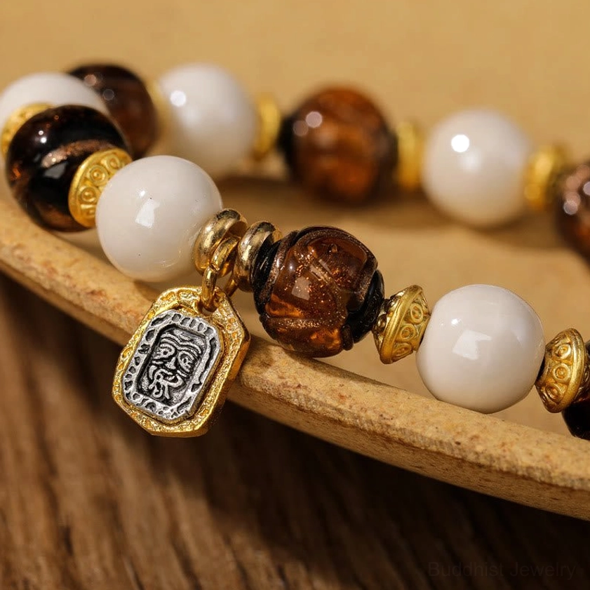 Macro close-up of Goddess of Wealth bracelet beads showing glossy white porcelain, textured dark glass beads, and detailed gold pendant