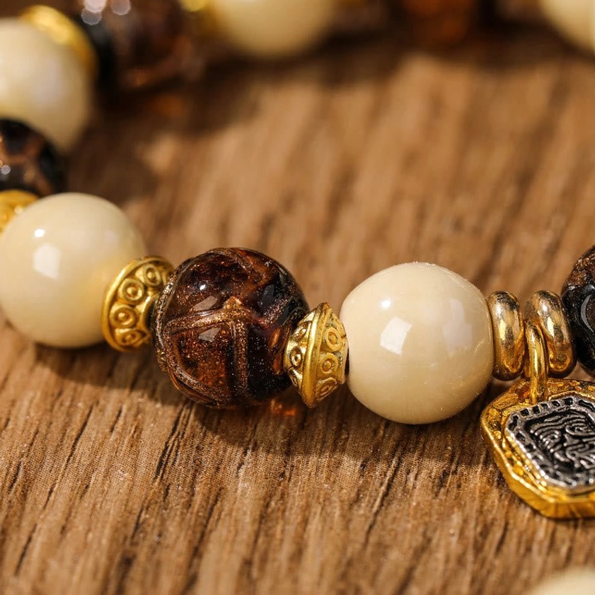 Extreme close-up of Goddess of Wealth bracelet components featuring marbled brown beads, cream porcelain, and gold-framed charm