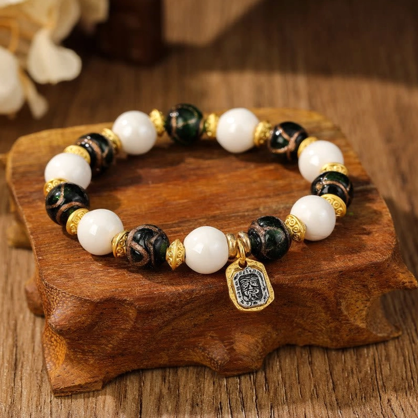 Close-up of single Goddess of Wealth bracelet featuring white porcelain beads, dark striped glass beads, and gold metal charm