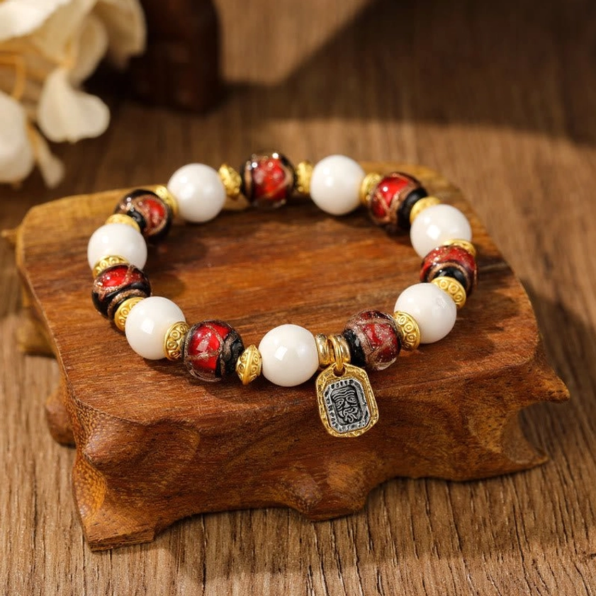 Goddess of Wealth spiritual bracelet with white porcelain beads, red patterned ceramic beads, and engraved metal pendant