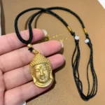 Gold Buddha head copper pendant necklace with black woven rope and white bead accents, close-up handheld view